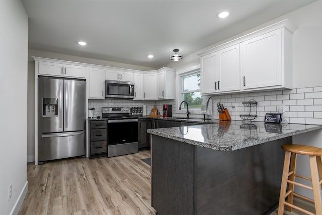 kitchen featuring white cabinets, appliances with stainless steel finishes, a sink, dark stone countertops, and a peninsula