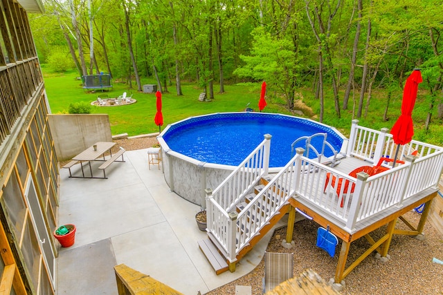 7751 W Old Barclay Creek Ln, Columbia, MO 65202 - swimming pool featuring a lawn, a patio, a trampoline, a view of trees, and a wooden deck