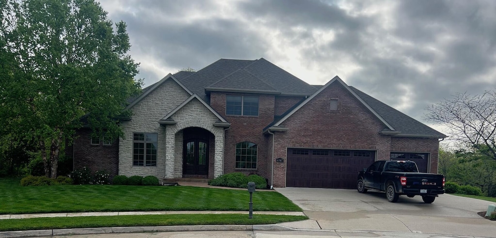 view of front facade featuring brick siding, a front lawn, an attached garage, and driveway