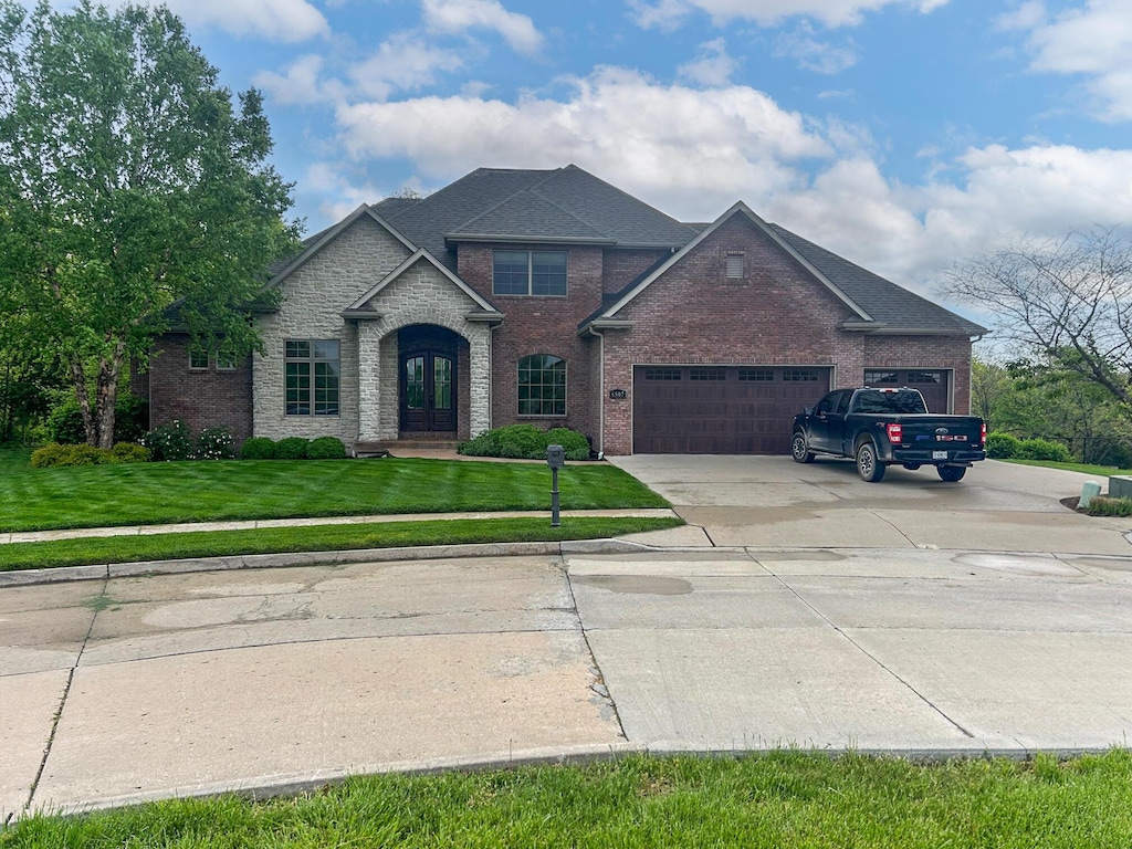 traditional home with a front lawn, brick siding, a garage, concrete driveway, and french doors