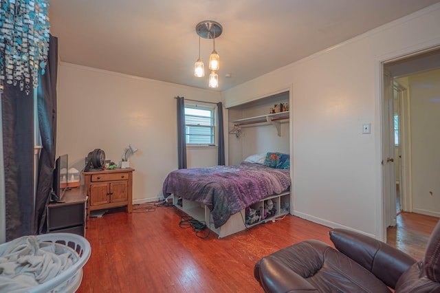 bedroom with baseboards, ornamental molding, a closet, and wood finished floors