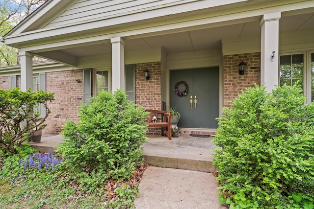doorway to property with covered porch and brick siding