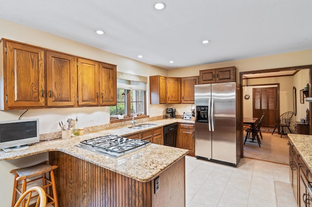 kitchen featuring brown cabinets, light stone countertops, a sink, stainless steel appliances, and a peninsula