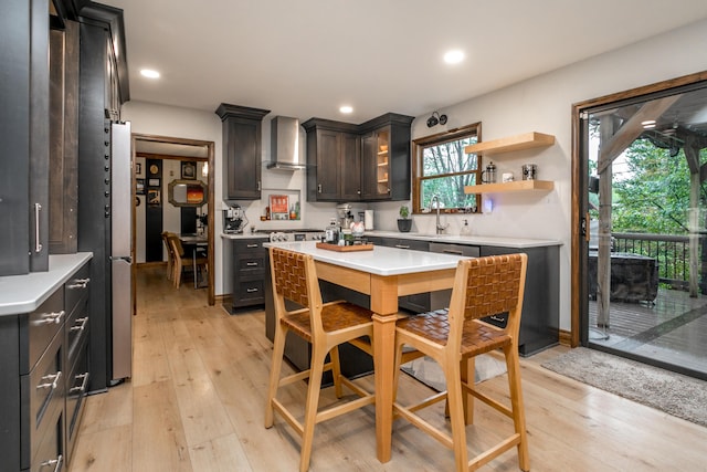 kitchen with wall chimney range hood, a sink, light wood finished floors, light countertops, and recessed lighting