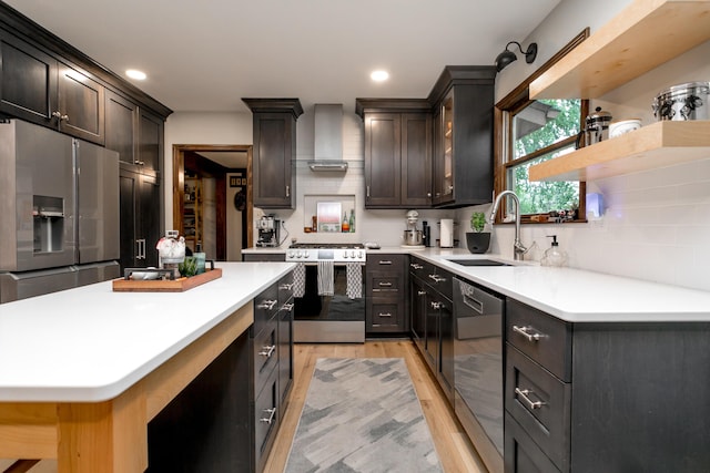 kitchen featuring open shelves, wall chimney exhaust hood, a sink, stainless steel appliances, and light wood-style flooring