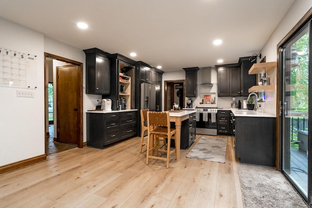 kitchen featuring open shelves, light countertops, dark cabinets, wall chimney exhaust hood, and stainless steel range with gas cooktop