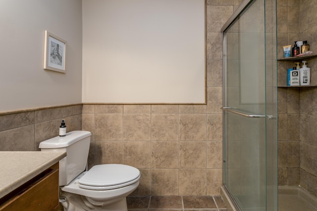 bathroom with vanity, toilet, a wainscoted wall, tile walls, and a stall shower