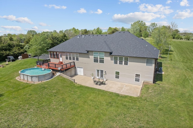 rear view of property featuring a lawn, a wooden deck, a shingled roof, and a patio area