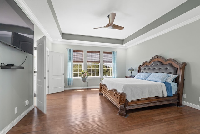 bedroom featuring a ceiling fan, wood finished floors, baseboards, ornamental molding, and a tray ceiling
