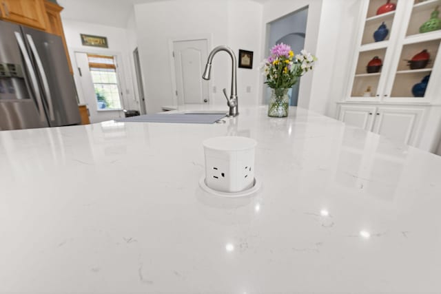 details with a sink, stainless steel fridge with ice dispenser, and light stone counters