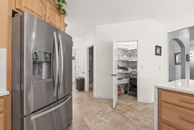 kitchen featuring stainless steel refrigerator with ice dispenser, arched walkways, baseboards, and light countertops