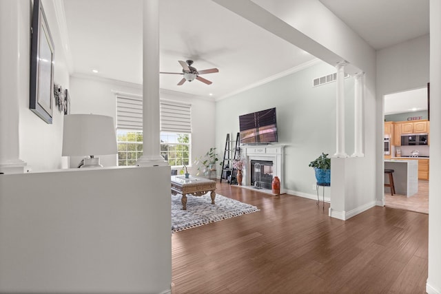 living area with crown molding, ceiling fan, decorative columns, and wood finished floors