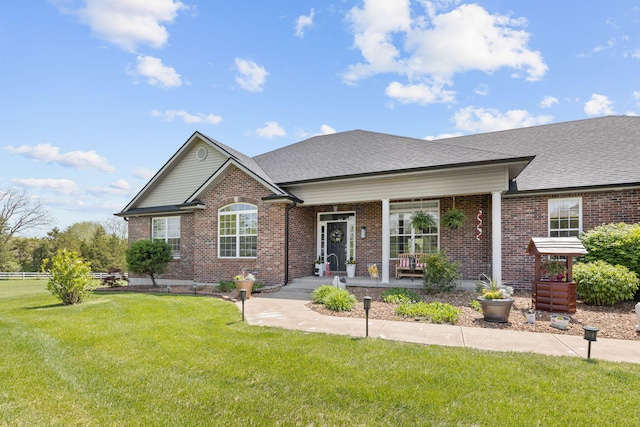 view of front facade featuring brick siding, a shingled roof, a front yard, and a porch