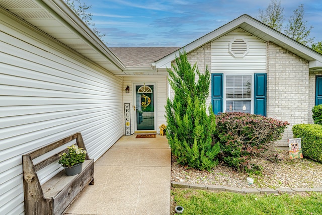 doorway to property with brick siding and roof with shingles