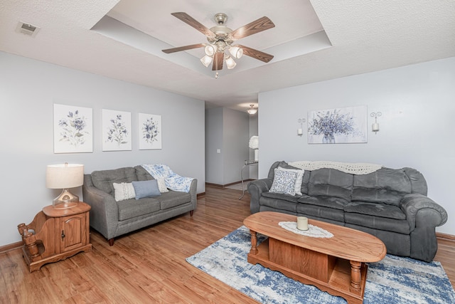 living room featuring ceiling fan, visible vents, baseboards, and light wood-type flooring