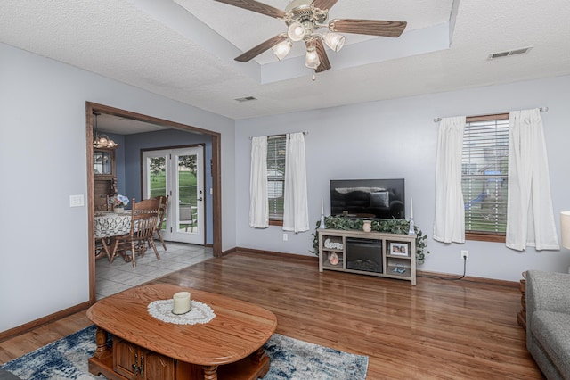living room featuring baseboards, light wood-style floors, ceiling fan with notable chandelier, and visible vents