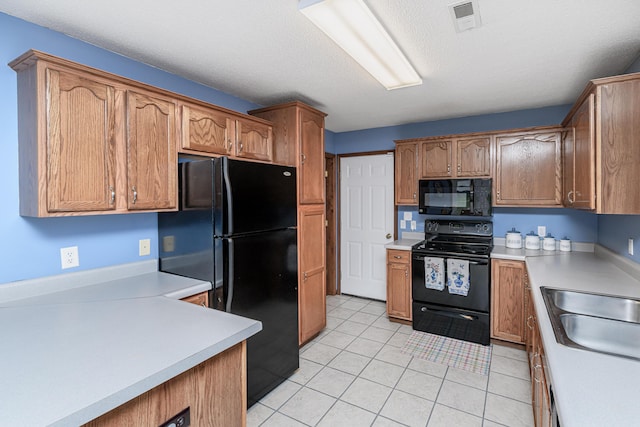 kitchen with a sink, light countertops, light tile patterned floors, visible vents, and black appliances