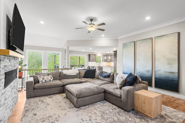 living room featuring crown molding, a stone fireplace, recessed lighting, a ceiling fan, and light wood finished floors