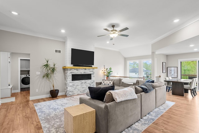 living room featuring washer / clothes dryer, a ceiling fan, a stone fireplace, and ornamental molding