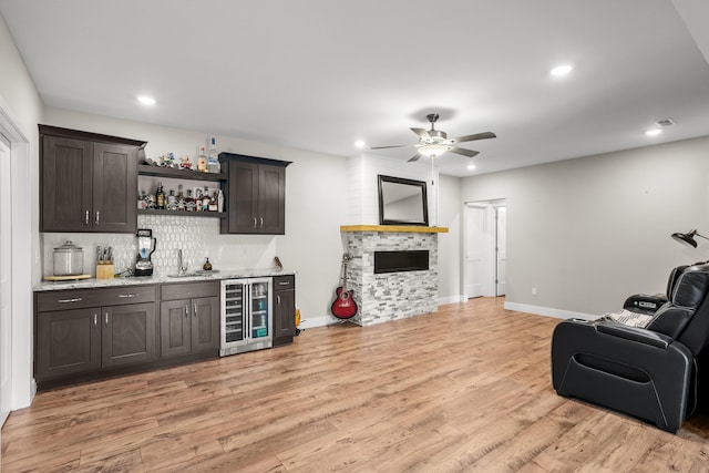 living area with beverage cooler, light wood-style floors, baseboards, ceiling fan, and indoor wet bar
