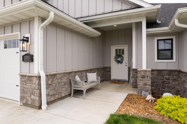 view of exterior entry featuring roof with shingles, stone siding, and a garage