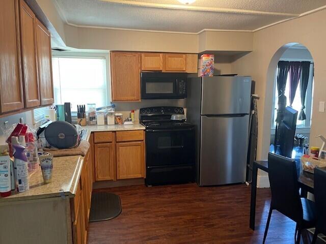 kitchen featuring brown cabinetry, dark wood-style floors, light countertops, arched walkways, and black appliances