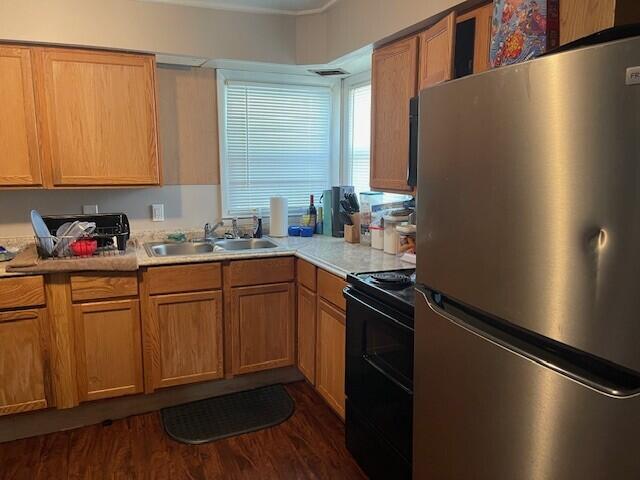 kitchen featuring freestanding refrigerator, light countertops, a sink, dark wood finished floors, and black / electric stove