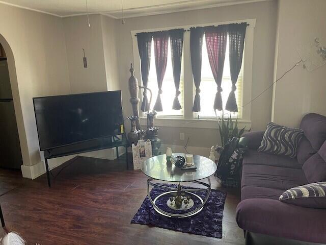 living room featuring arched walkways, ornamental molding, and wood finished floors