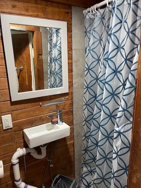 full bathroom featuring wooden walls, a shower with curtain, and a sink