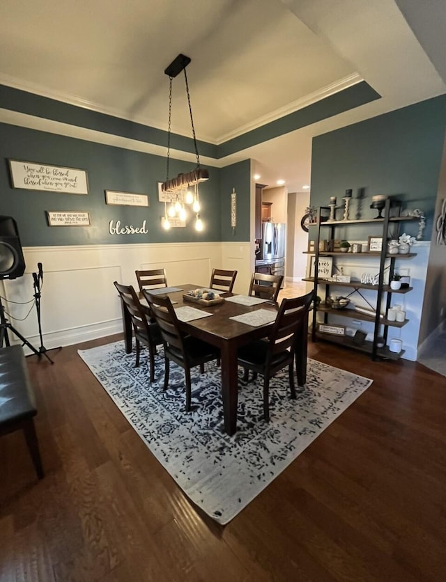dining space featuring crown molding, a raised ceiling, a wainscoted wall, and dark wood finished floors