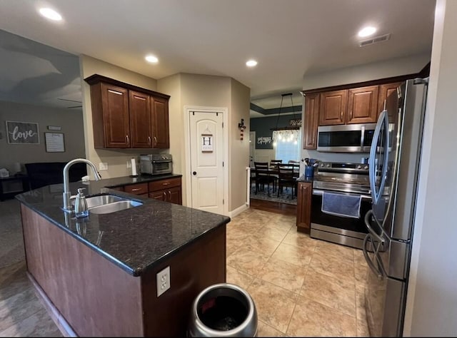 kitchen featuring a sink, dark stone counters, stainless steel appliances, a peninsula, and visible vents