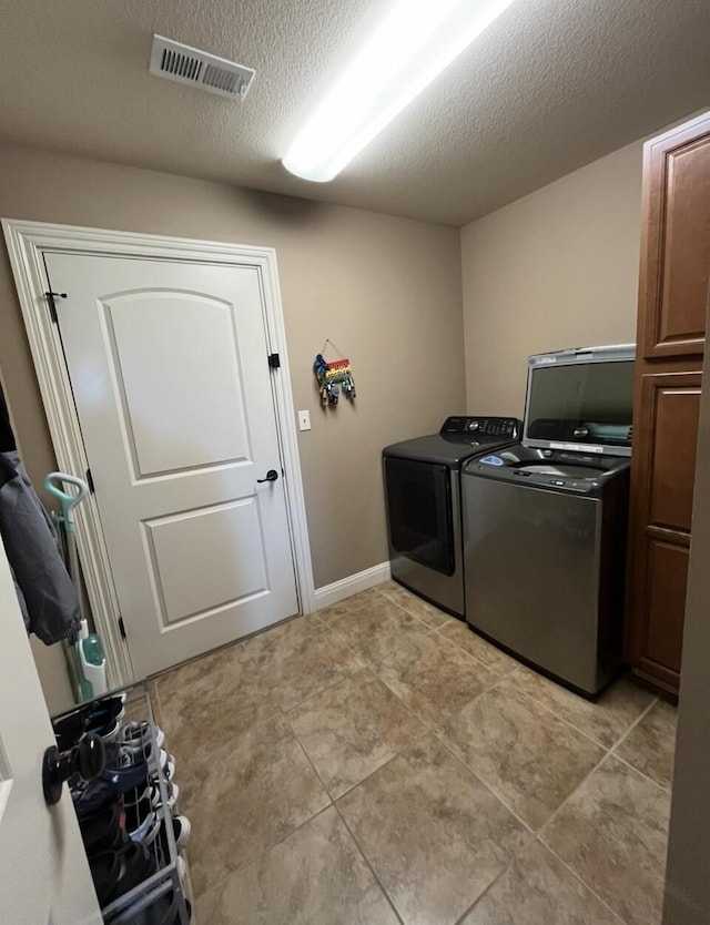 laundry room featuring cabinet space, light tile patterned flooring, a textured ceiling, visible vents, and washer and clothes dryer