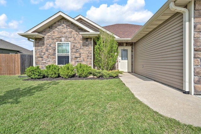 doorway to property with fence, a lawn, and stone siding
