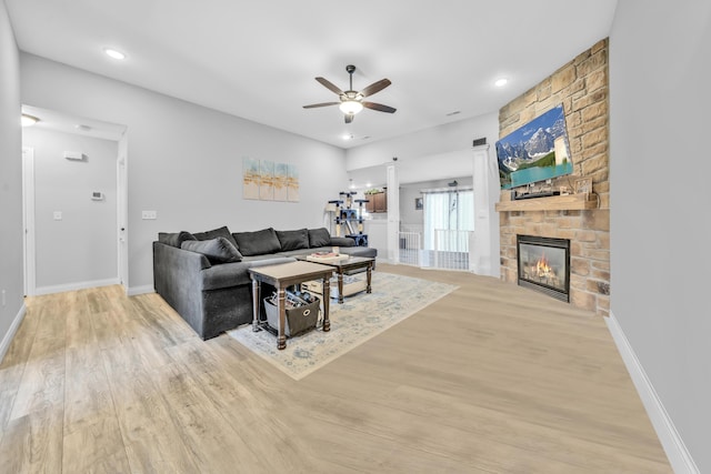 living room with light wood-style floors, a stone fireplace, a ceiling fan, baseboards, and recessed lighting