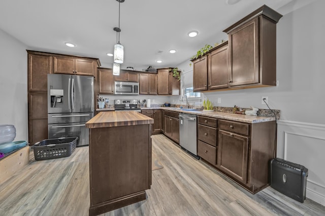 kitchen featuring butcher block countertops, light wood-type flooring, a sink, appliances with stainless steel finishes, and decorative light fixtures