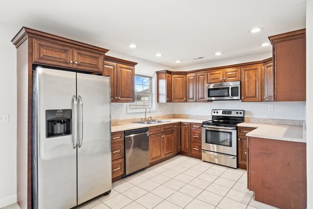 kitchen with brown cabinetry, appliances with stainless steel finishes, a sink, light tile patterned floors, and light countertops