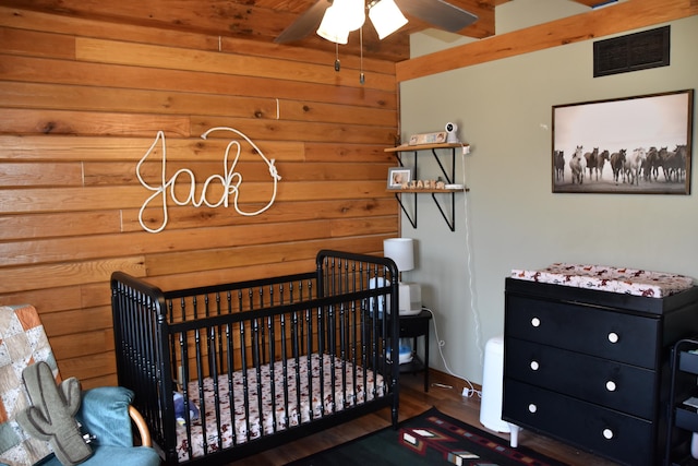 bedroom with a nursery area, wood walls, wood finished floors, and visible vents