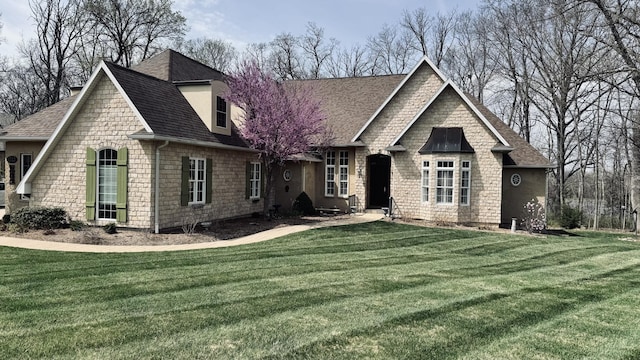 view of front of home with a front lawn, roof with shingles, and stone siding