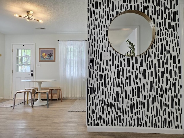 interior space with baseboards, a textured ceiling, wood finished floors, and visible vents