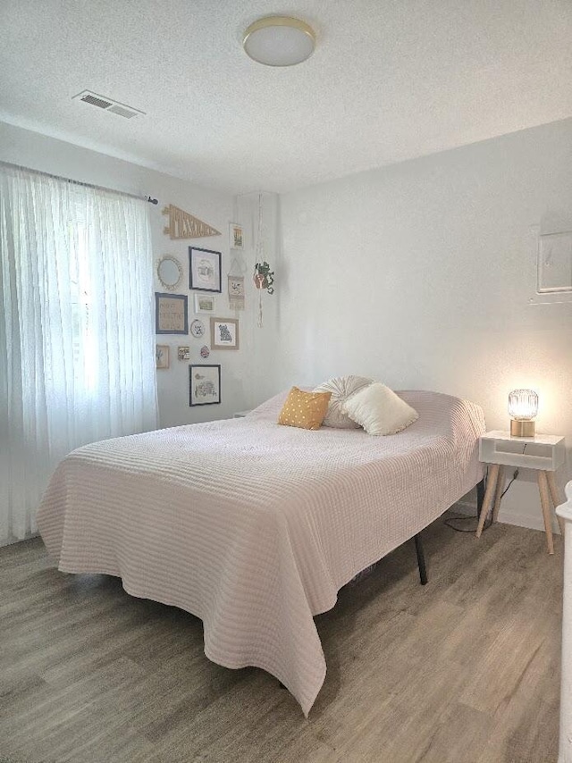 bedroom featuring visible vents, a textured ceiling, and wood finished floors