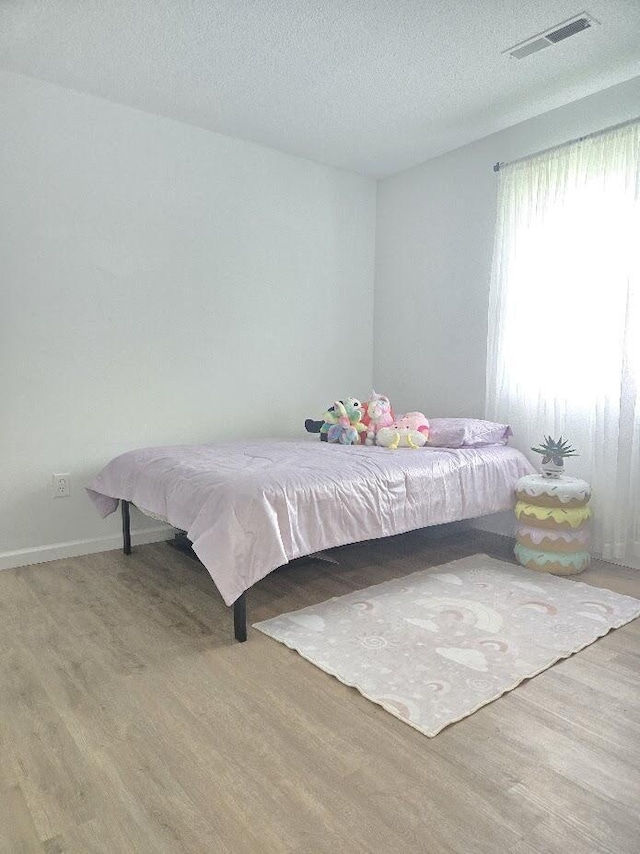 bedroom featuring a textured ceiling, baseboards, wood finished floors, and visible vents