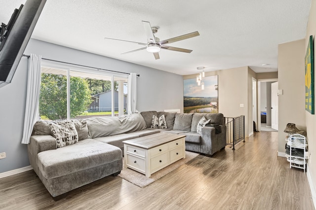 living room featuring ceiling fan, light wood finished floors, baseboards, and a textured ceiling