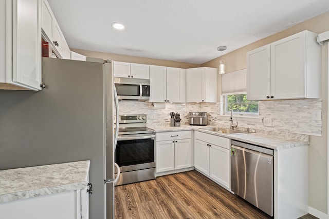 kitchen with stainless steel appliances, a sink, dark wood-type flooring, white cabinets, and decorative backsplash