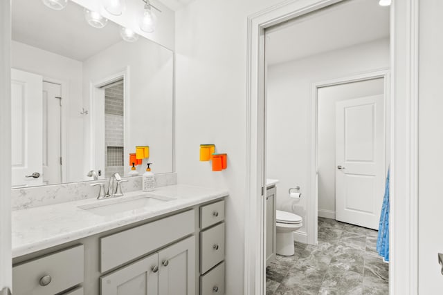 bathroom featuring toilet, vanity, marble look tile flooring, and baseboards