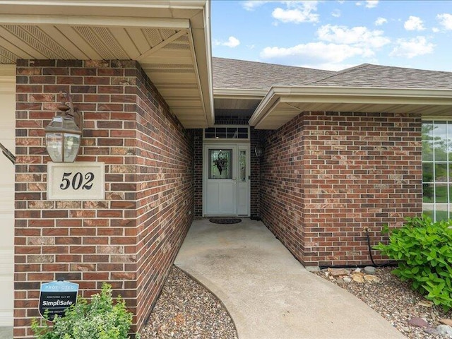 view of exterior entry with brick siding and roof with shingles