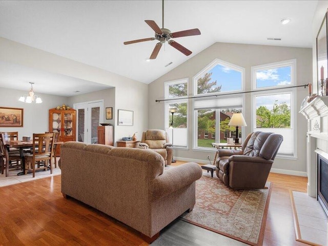 living room with a tile fireplace, light wood finished floors, plenty of natural light, and ceiling fan with notable chandelier