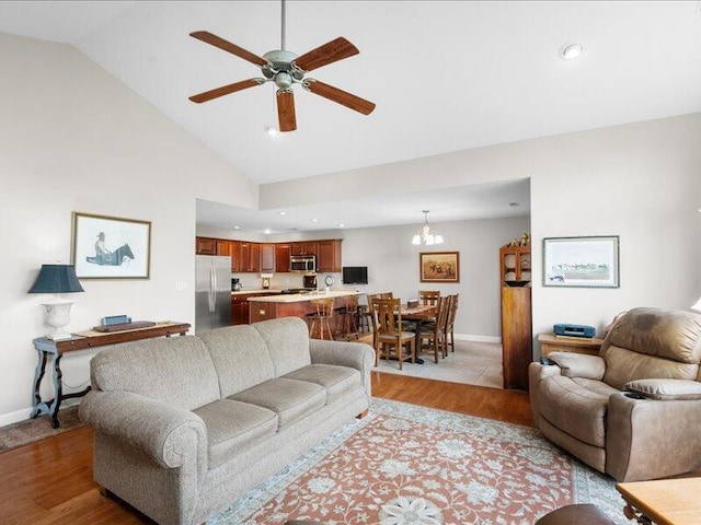 living room featuring lofted ceiling, recessed lighting, baseboards, ceiling fan with notable chandelier, and light wood-type flooring