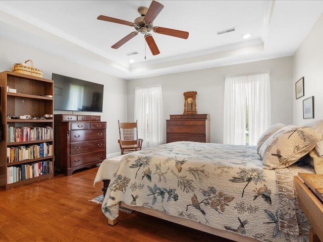 bedroom with a raised ceiling, multiple windows, visible vents, and wood finished floors