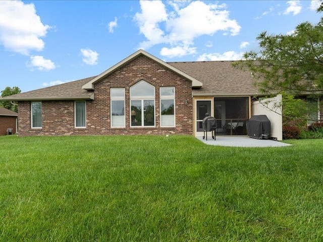 rear view of house with a shingled roof, a patio, and a lawn