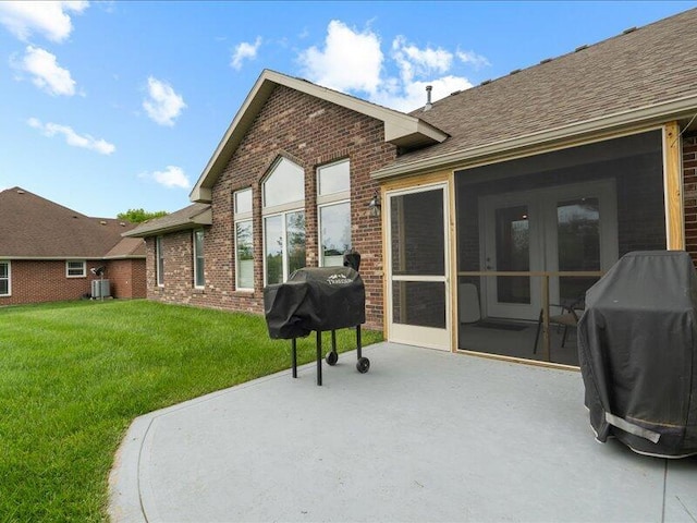 back of property featuring brick siding, roof with shingles, a lawn, and a patio area